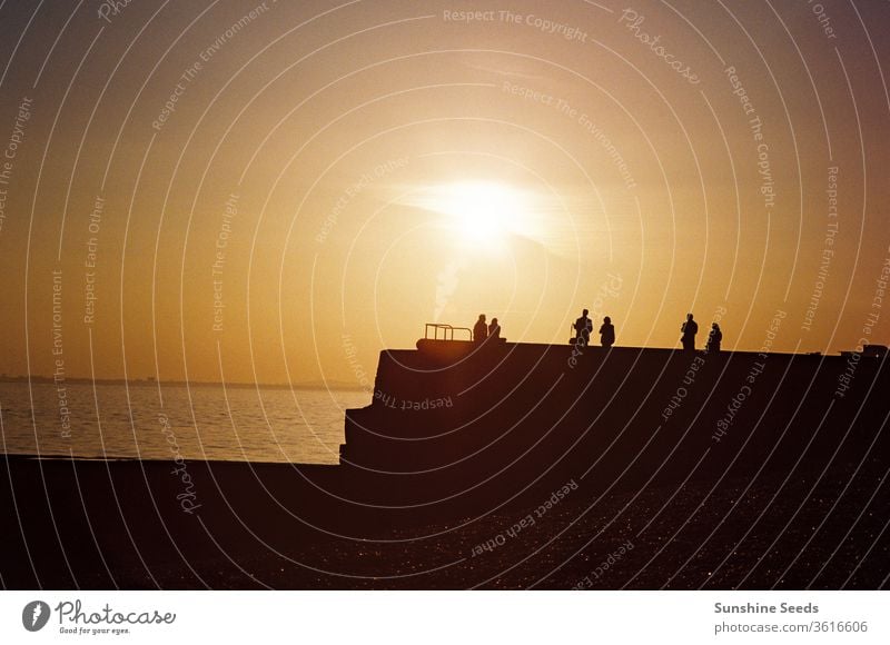 Silhouette of people on break water wall on beach at sunset seaside orange yellow moody dramatic sky sunrise ocean