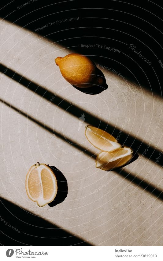 A whole, a half and two quarters of lemon on grey background with shadow stripes and lines. Harsh sunlight and high contrast concept for creative and healthy projects.