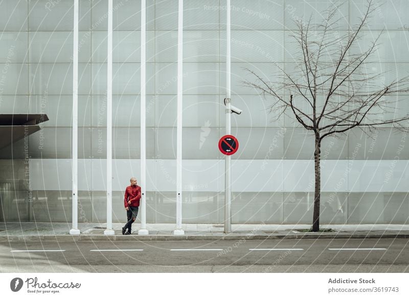 Young man standing near modern building young style casual wall urban street trendy prohibit sign male contemporary alone youngster street style gray