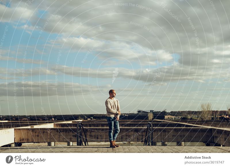 Young man standing on concrete construction on street stone shabby urban alone sky cloudy hipster modern guy casual male confident contemporary individuality