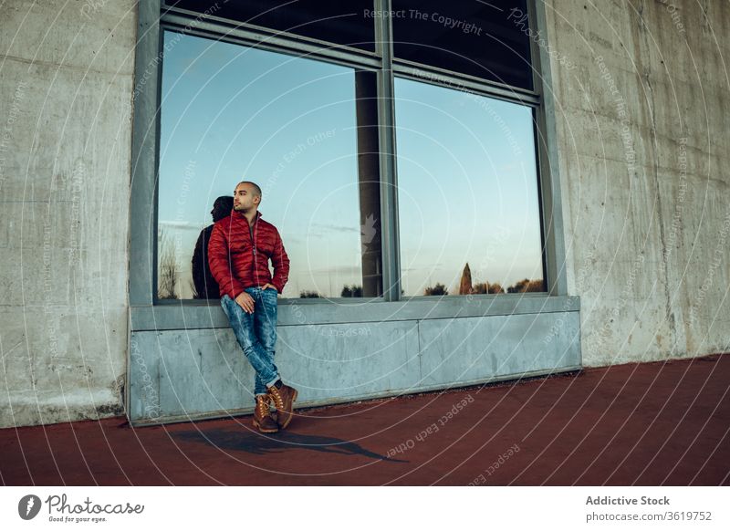 Young man in trendy outfit standing on street young modern confident jacket warm clothes pensive hipster unshaven autumn beard thoughtful think bald male