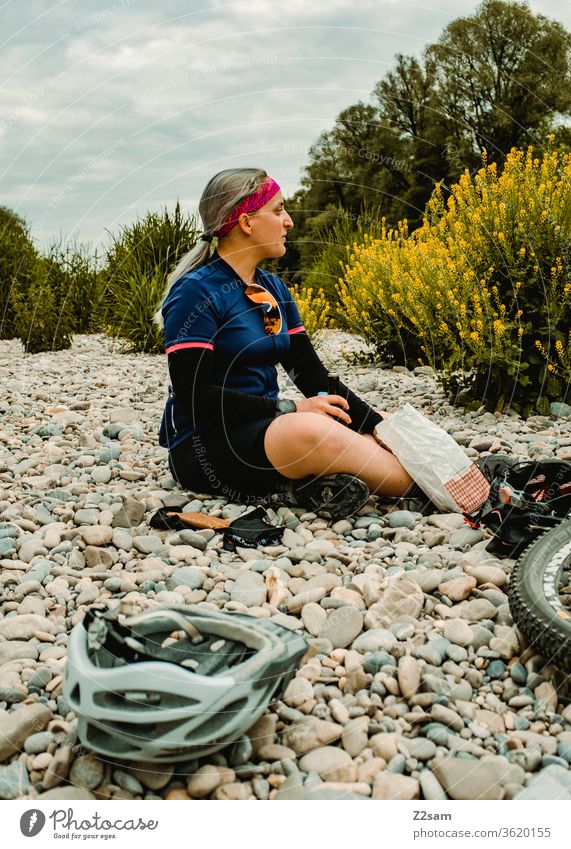 Break on the bike tour Isar Beach Sit Relaxation Cycling Sports athlete Eating snack Baker Helmet mtb Mountain bike Jersey Sunglasses Nature Landscape Summer