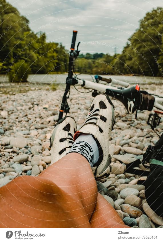 Young man takes a break with his MTB mtb Mountain bike Beach Isar River Nature Sportsperson Legs Athlete Bicycle ride a bike recover Exterior shot Cycling