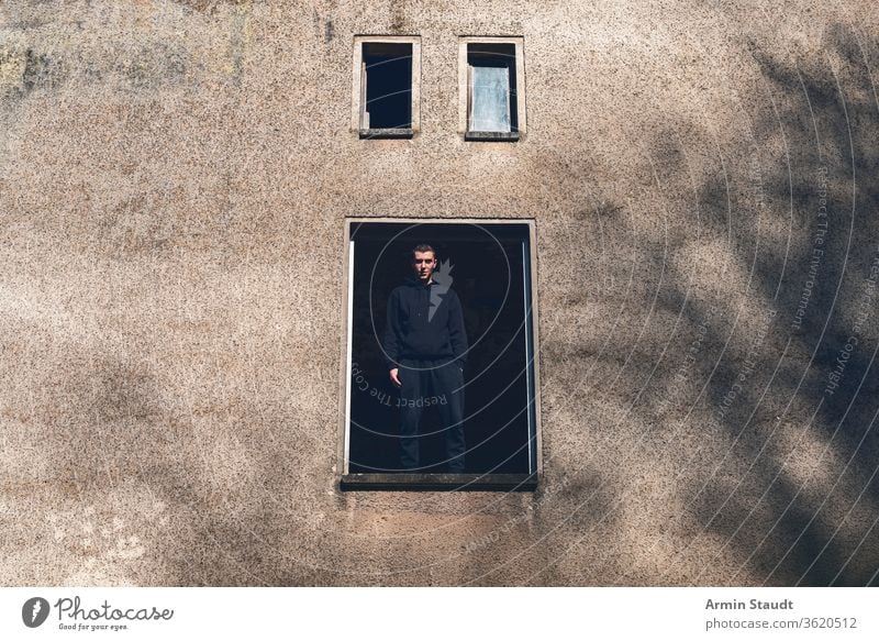 smiling young man stands in an open window of a house standing old ruin looking far wide hand distance black architecture building abandoned ancient blue sky