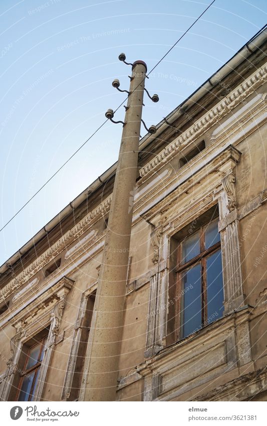 Partial view of a dilapidated building from the Gründerzeit with high windows from the frog's perspective and with an old electricity pylon in front of it