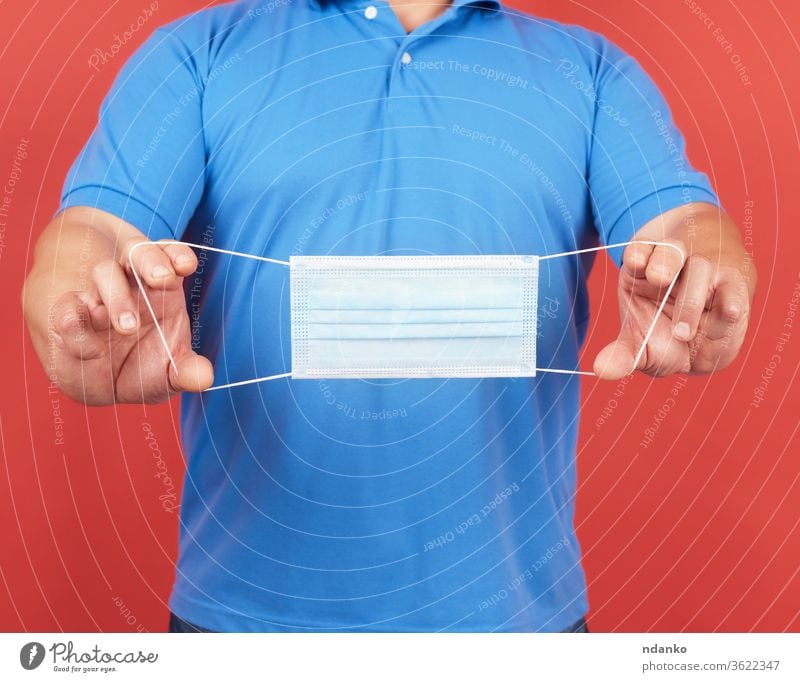 man in a blue T-shirt holds a stack of disposable medical white face masks medicine people person prevention protect protection quarantine red safety studio