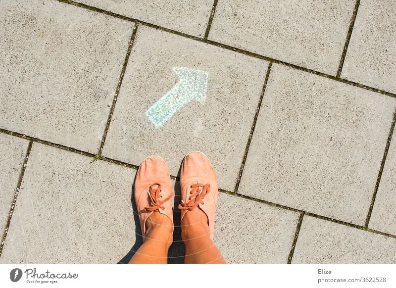 Feet stand in front of a green arrow painted on the floor with chalk. Signpost, direction, decision support. Road marking Direction Decide off Correct Arrow