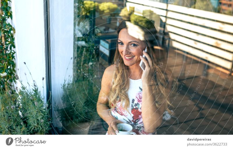 Woman talking on the cellphone with coffee cup woman cell phone through the glass reflection window beverage watching the views break tea looking elegant happy