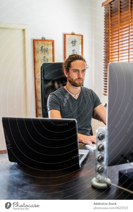 Handsome man working at desktop computer at home typing keyboard freelance remote using male serious project busy gadget device monitor screen watch job