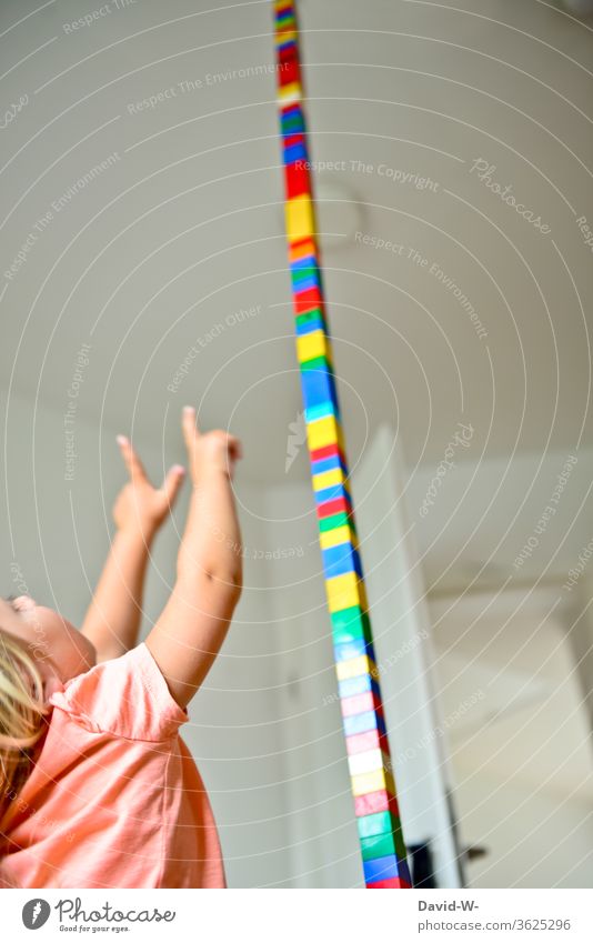 Child builds a huge tower with building blocks in the children's room and points enthusiastically with his fingers at the ceiling Build Tower Building bricks