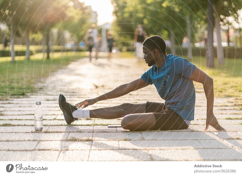 Athletic black man exercising at the park male fitness workout sport runner warming up flexibility healthy lifestyle stretching athlete young training body