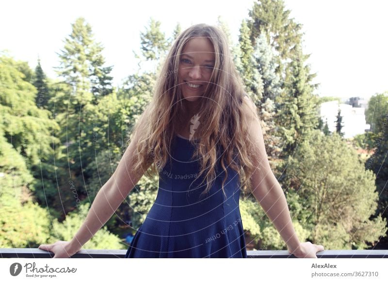 Portrait of a laughing young woman on the balcony in front of trees Blue sky huts Intensive girl Adults portrait Day Skin Sunlight Self-confident