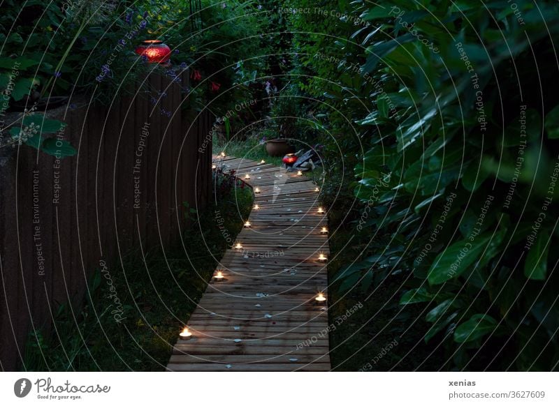 On the wooden path in the garden many candles are lit and spread a romantic atmosphere in the evening. Two pot-bellied lamps set red accents. Garden off