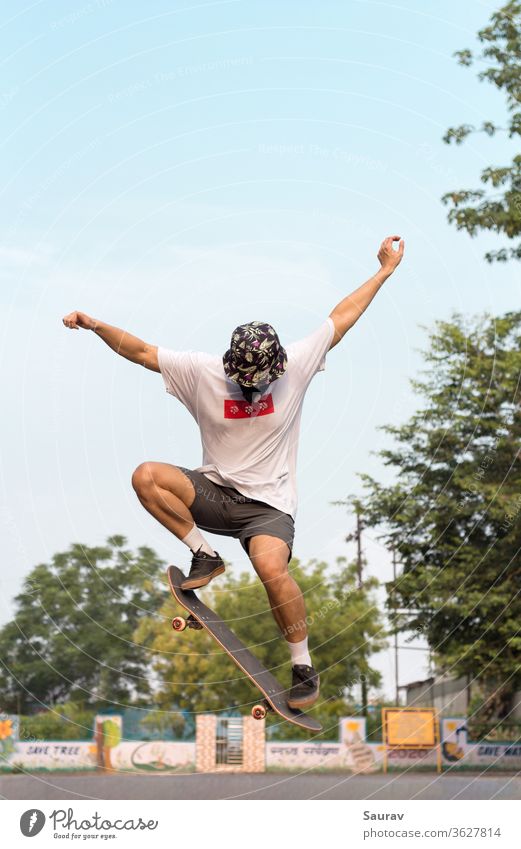 A Young Adult wearing a protective mask to avoid Coronavirus infection while doing an Ollie stunt on his Skateboard outdoors ion an empty road. summer