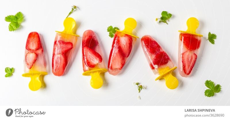 Homemade strawberry popsicles frozen juice, ice cream on sticks and fresh green leaves on white background. Bright refreshing taste of summer, banner dessert