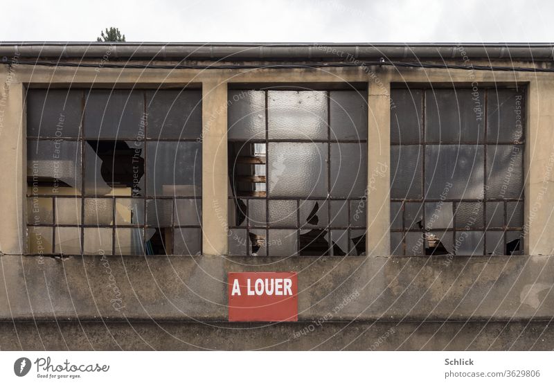 Facade of a dilapidated industrial building with broken windows and red sign a louer for rent Industry Window corrupted Broken Text for hire Sky Tree tops Hope