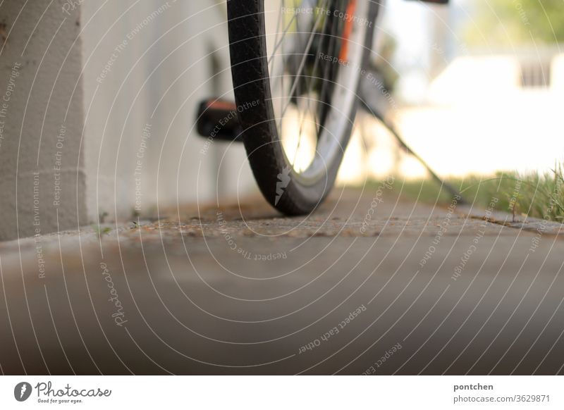 A bicycle stands in front of a house. View from below. Partial view. Tires, pedal, bicycle stand Bicycle Pedal Bicycle rack turned off Mobility Summer Sunlight