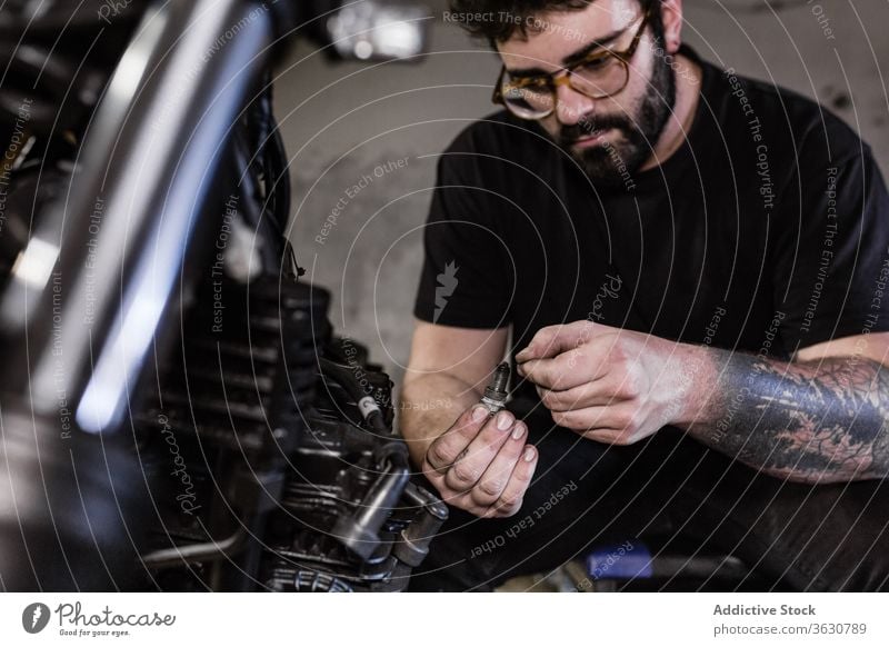 Bearded man fixing spark plug of motorcycle mechanic garage dirty motorbike male repair vehicle workshop serious maintenance service job transport equipment guy