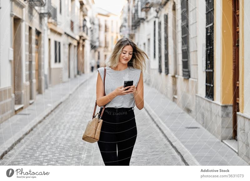 Positive young woman with smartphone walking on street city using happy style message browsing female mobile lifestyle device gadget stroll urban smile trendy