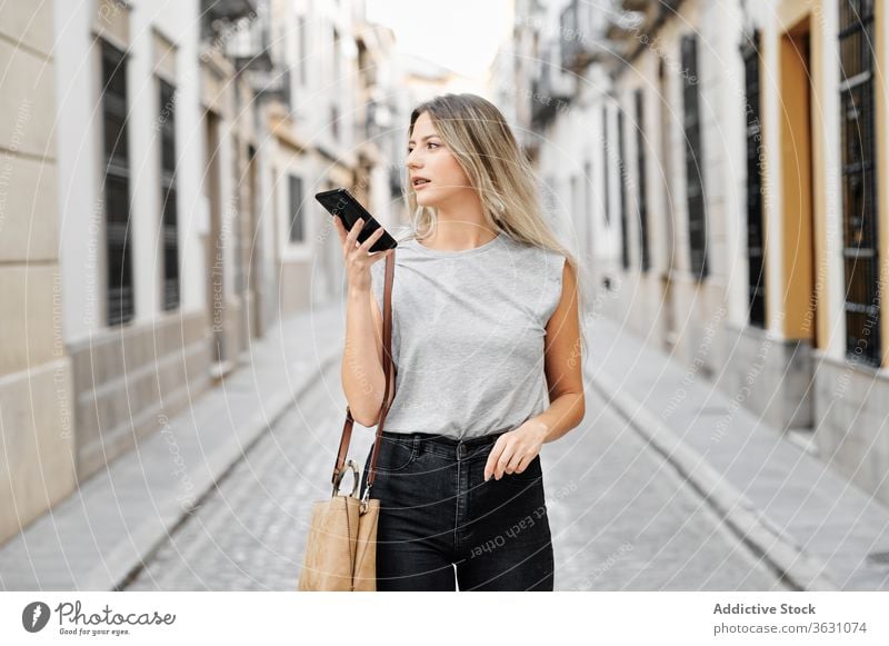 Positive young woman with smartphone walking on street city using happy style message browsing female mobile lifestyle device gadget stroll urban smile trendy