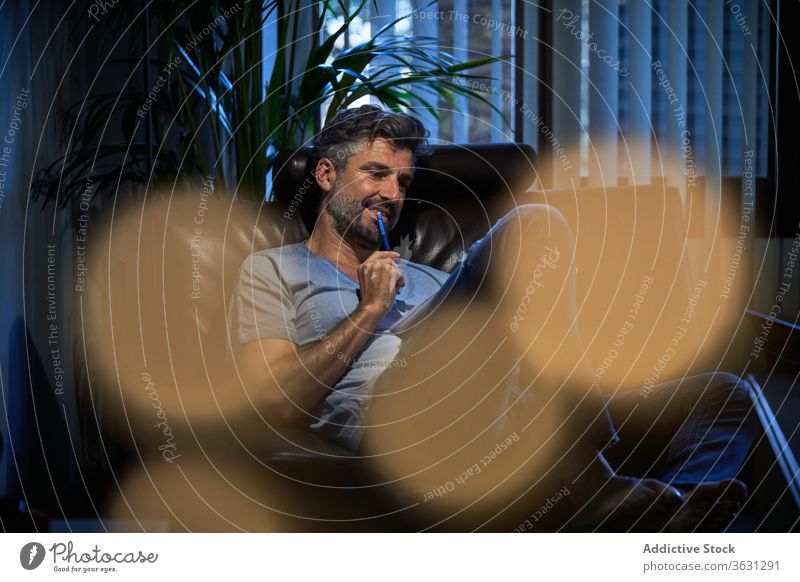 Relaxed man reading notes in notebook take note notepad mature comfort cheerful relax male rest armchair casual smile smart glad joy positive cozy apartment