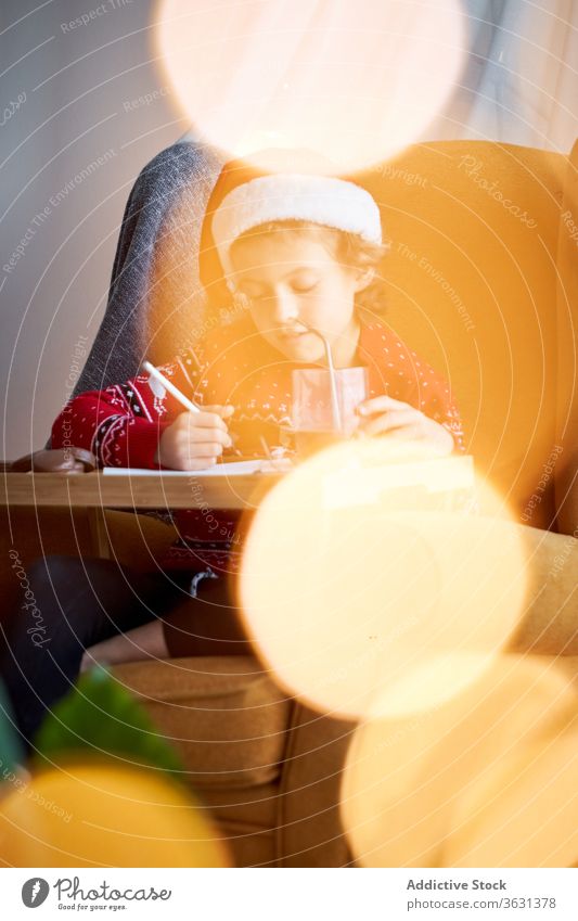 Happy boy in Christmas wear sitting in cozy armchair santa hat christmas holiday pencil happy comfort domestic sweater glad cheerful comfortable bokeh positive