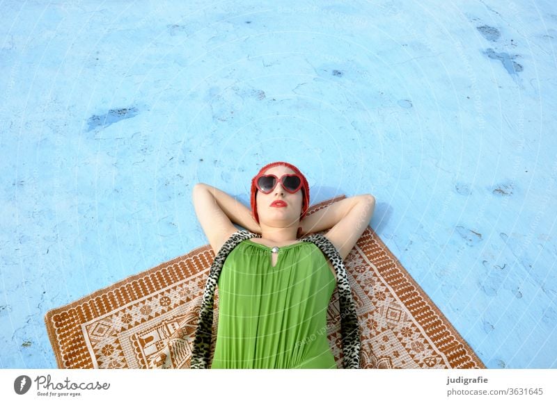 The girl with the beautiful red bathing cap and green swimsuit is sunbathing in the empty non-swimmer's pool. A summer love. Girl Woman Swimwear Bathing cap