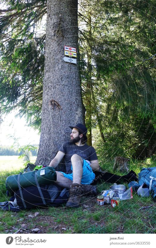 The man sits leaning against the tree and takes a break from hiking, while he thinks about what a long way lies ahead with his heavy backpack. Man Nature Forest