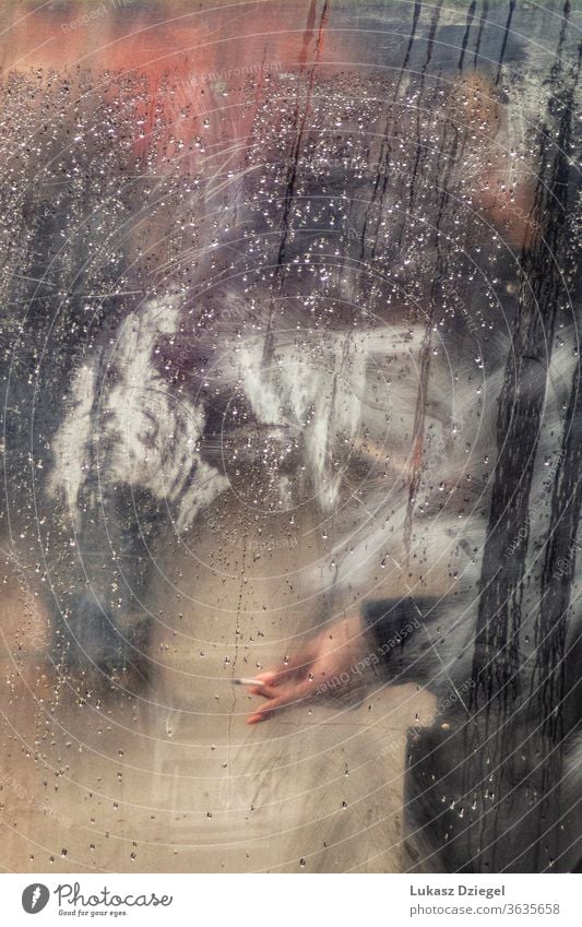 Hand with cigarette in the window full of raindrops at the rainy day street cigarette smoking blurry droplet weather shape condensation urban texture smoke