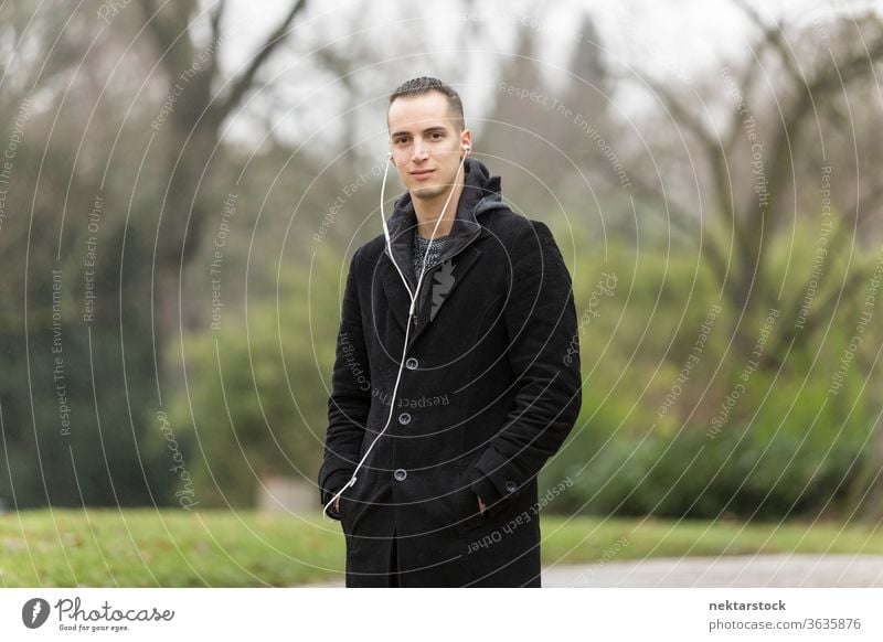 Young Man with Earphones Posing in Autumn Park man portrait caucasian ethnicity earphones outdoors medium shot natural lighting day fashion coat button-down