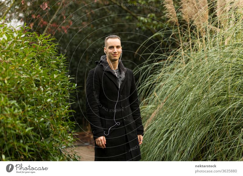 Man with Earphones and Black Coat Posing in Botanical Garden man portrait caucasian ethnicity earphones outdoors medium shot natural lighting day fashion coat