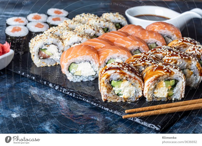 A box of sushi Nigiri, Uramaki California, Philadelphia, on a black stone plate. Sushi menu in a white transport box on a wooden background. nigiri cutlet beef