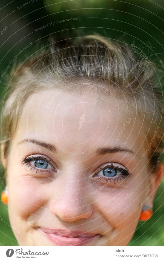 Pretty, young, roll-eyed, slippery woman with orange earrings and ponytail laughs mischievously into the camera. Summer outing with happy, optimistic, feminine, radiant teenager in nature. Portrait, face down slipped.