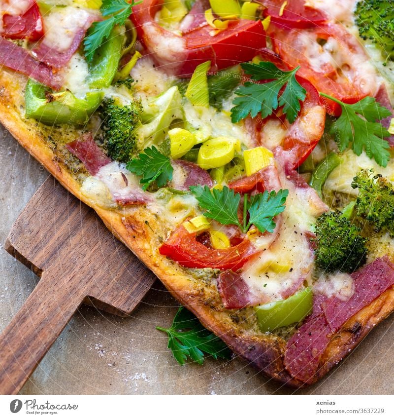 Seĺbstgebackene Pizza thickly topped with tomatoes, broccoli, leek, salami and of course lots of cheese on top. The big piece is taken from the baking paper with the wooden slider.