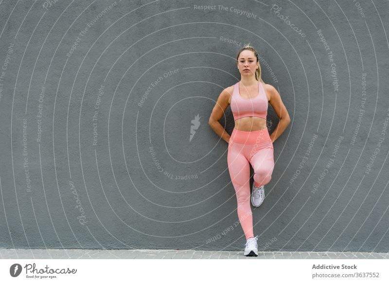 Sportswoman in active wear standing leaned on gray wall sportswoman lean on leg fit healthy wellbeing activewear harmony vitality leggings sneakers embankment