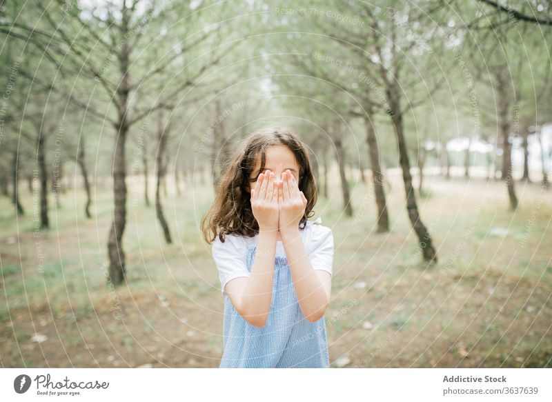 Unrecognizable girl standing on chair in alley between trees cover face park peaceful harmony barefoot hide concept casual dress child idyllic trunk youth