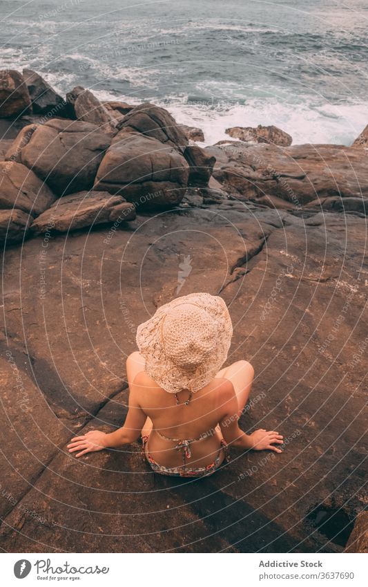 Anonymous traveling woman on rocky seashore holiday summer season admire tourist female stone spectacular seascape vacation nature idyllic tourism coast sit