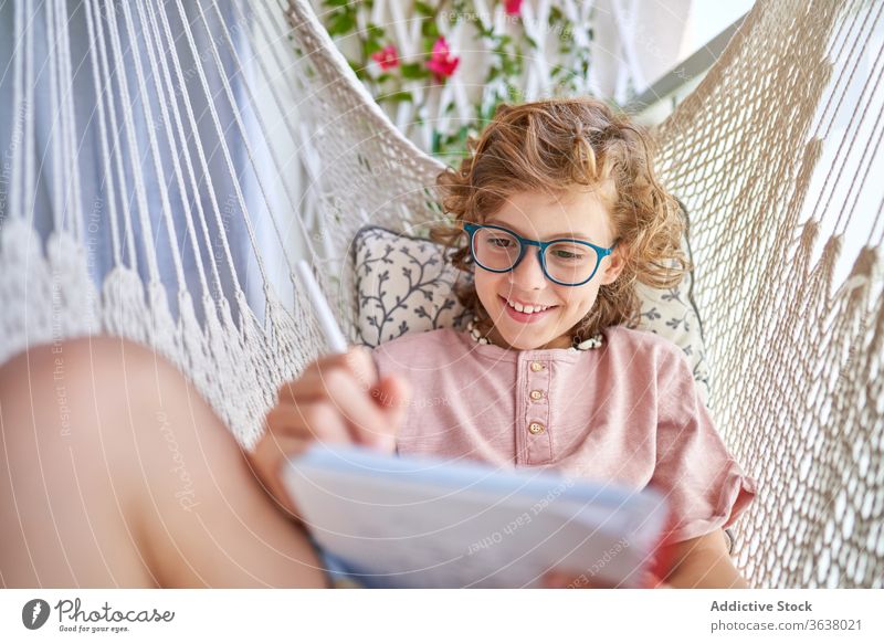 Schoolboy in eyeglasses studying in hammock with copybook at home schoolboy education homework knowledge intelligent focused pencil childhood comfort pensive