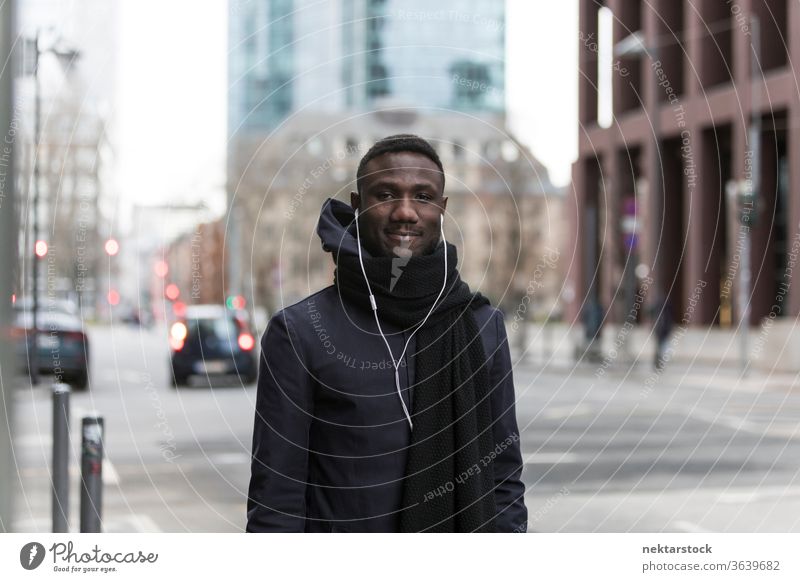 Handsome Black Man with Earphones Posing on Big City Street portrait earphones man African ethnicity smiling black coat autumn street listening music audiobook