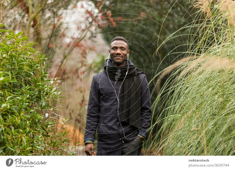 Happy Black Man with Earphones Posing in Park portrait earphones man African ethnicity black autumn leaf color grass tall public park listening music audiobook