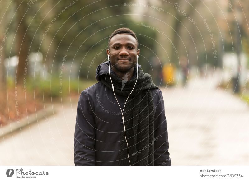 Young Man Listening to Earphones Smiling Confidently at Camera portrait earphones man African ethnicity black public park road trail listening music audiobook