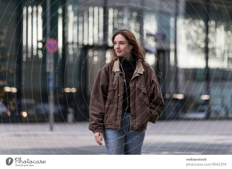 Young Woman Listening to Earphones with Hear Turned Away From Camera caucasian ethnicity woman female earphones audio music listening sidewalk street