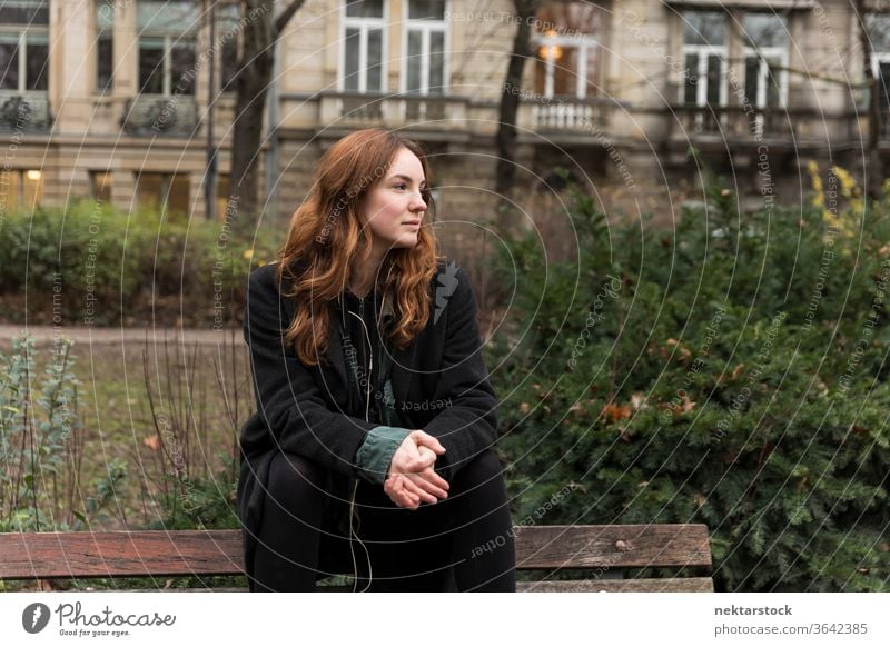 Young Caucasian Woman Sitting on Park Bench with Head Turned caucasian ethnicity woman female earphones audio music listening brown hair real life model