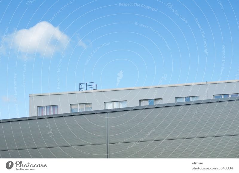 View across a grey functional building to an office building with windows in partial view in front of a blue sky with a single cloud Office building Window