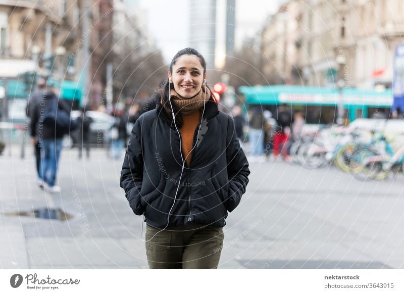 Young Indian woman walking on street listening to earphones and smiling at camera. young woman Indian ethnicity music medium shot audiobook focus on foreground