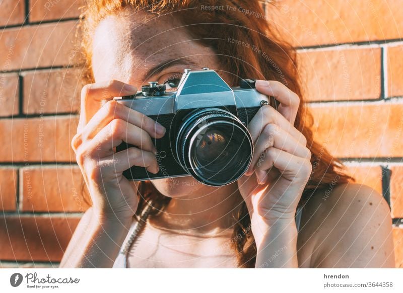 young woman holds an analog camera and looks through the viewfinder antiquated antique antiquity classic classical click close up electronic equipment film