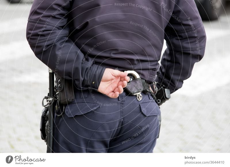 armed policeman with handcuffs from behind, partial view Police Force Police Officer Belt ready for use by hand Back Truncheon Handgun Handcuff standing gear