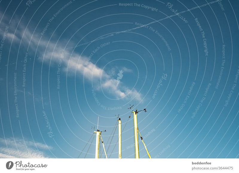 Tips of three white sailing masts with radio tracking and radar systems against a blue sky with feather cloud and contrails, both crossing each other Blue sky