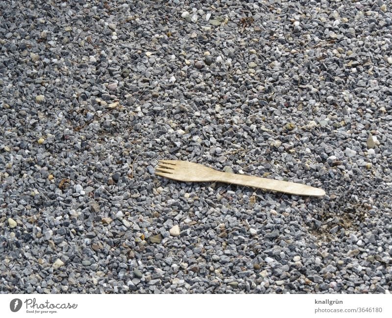 Organic disposable cutlery fork made of wood lies on road gravel Organic produce ecologic Environment environmental awareness Sustainability Nutrition natural