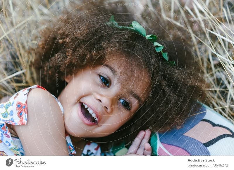 Cute ethnic little girl resting on wheat field mulatto black calm adorable summer trendy countryside cute forest outfit unemotional curly hair sunlight style